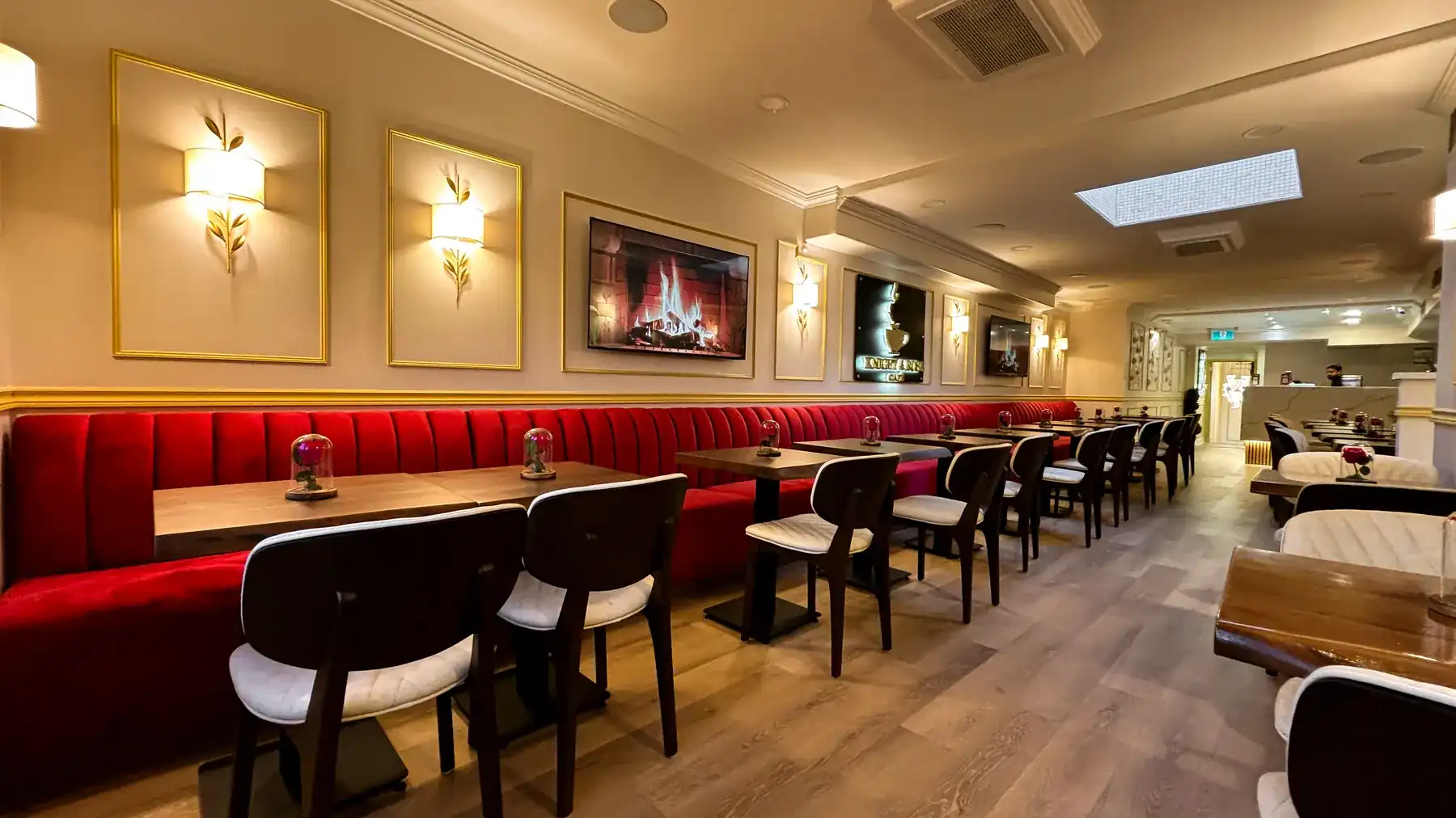 The long dining room of Knight & Rose Café in Streetsville, lit by gold wall sconces above red velvet banquettes.
